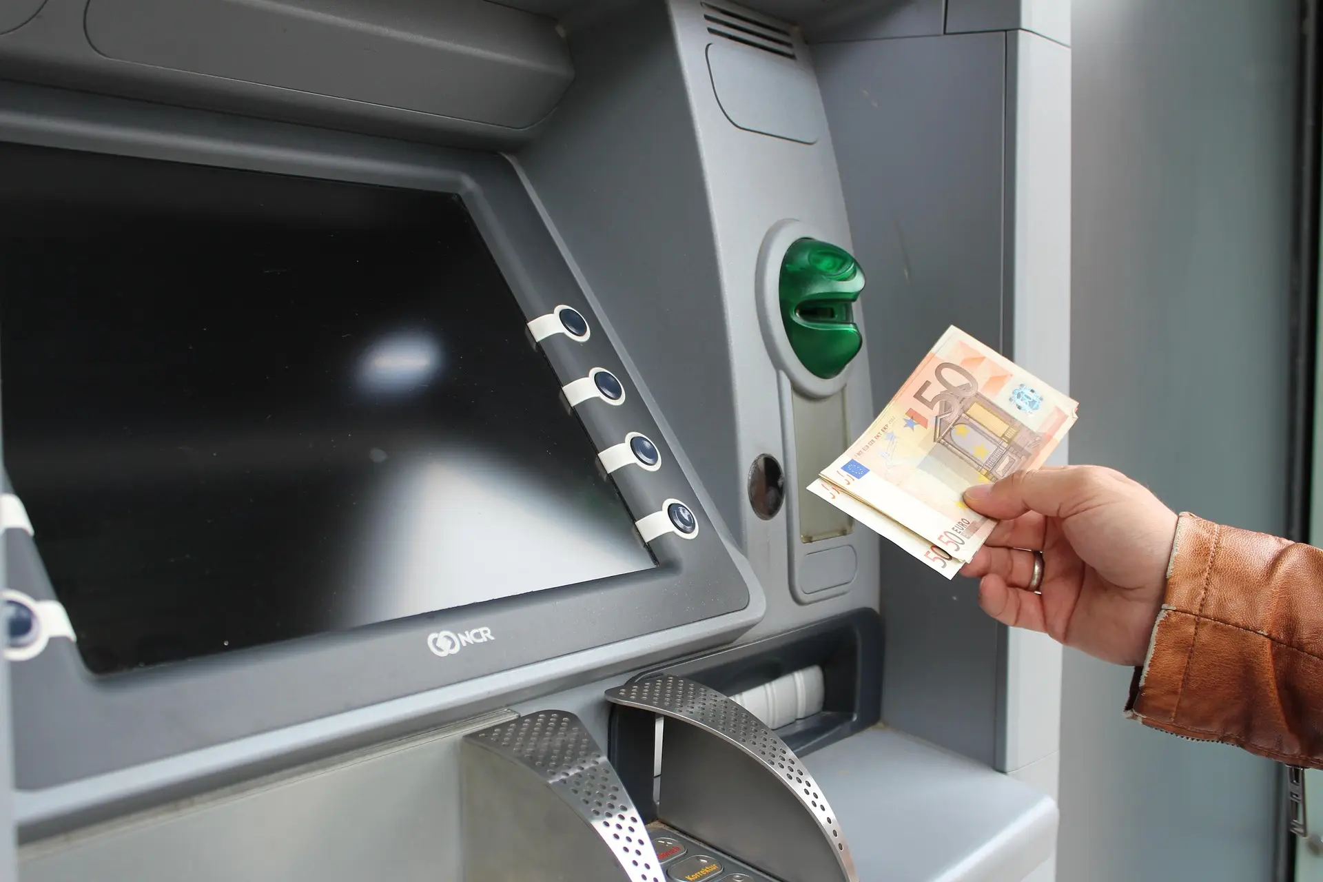 Hand mit einer Banknote vor einem Geldautomaten – an Bitcoin-Automaten wird Bargeld in Franken oder Euro gegen Krypto getauscht