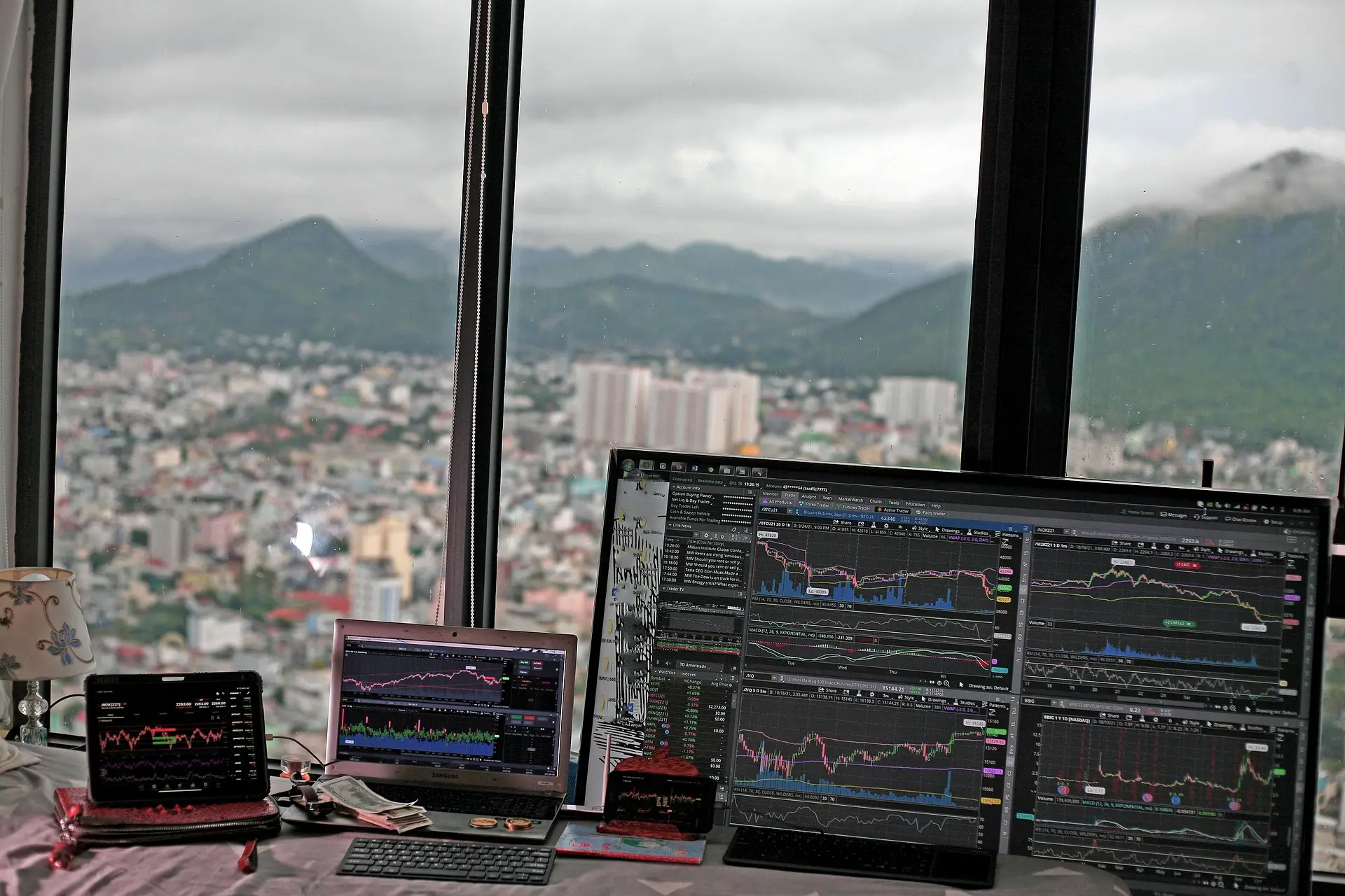 Più schermi con grafici dei prezzi davanti a una vetrata con vista su una città e colline – immagine simbolica per il trading di Solana (SOL)