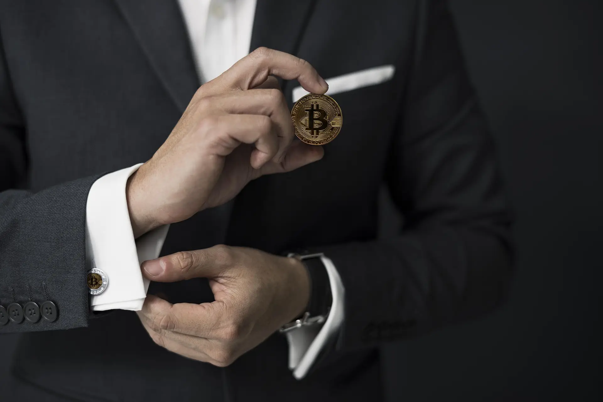 Mann im dunklen Anzug hält eine Bitcoin-Münze zwischen den Fingern – Symbolbild für grosse Krypto-Käufe über einen OTC-Desk