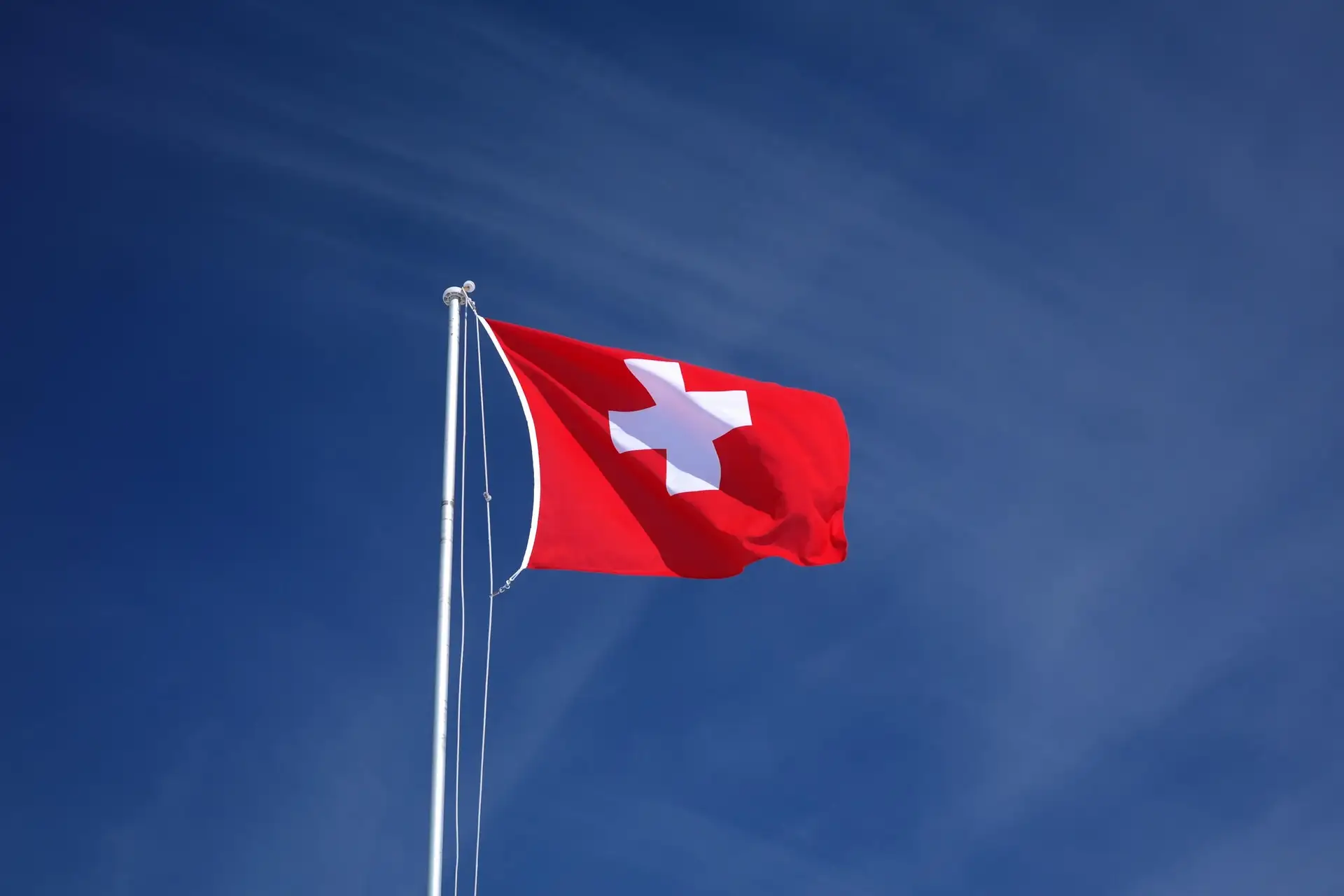 Schweizer Fahne an einem Mast vor blauem Himmel – Symbolbild für den Krypto-Standort Basel